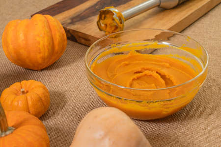 Pumpkin puree in a glass bowl, fresh pumpkin, squash, butternut close up on kitchen tableの写真素材