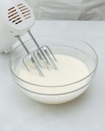 Whisked egg whites close up in a glass bowl, vertical banner. Baking process, step by step chocolate...