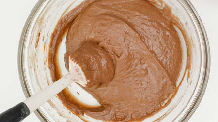 Chocolate cake recipe. Mixing cake batter in a glass bowl. Close up baking process, flat lay