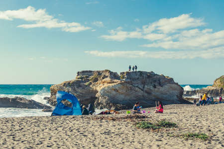 Montana de Oro, California, USA - March 6, 2021.  Rocky cliffs, sandy beach, and people enjoying...