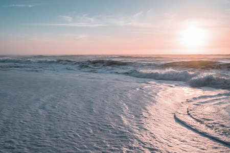 Seascape in light blue and pink colors. Sea waves and sun setting down the horizon. Peaceful scene,...