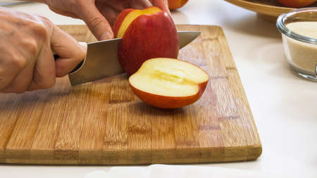 Woman cuts apples on a wooden cutting board. Close up on white kitchen table.の写真素材