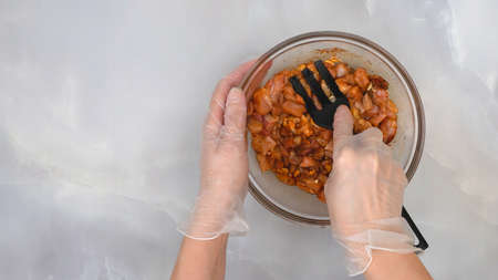 Sour cream chicken paprika recipe, step by step cooking process, part of series. Woman hands wearing gloves mixing marinated chicken fillet in a bowlの写真素材