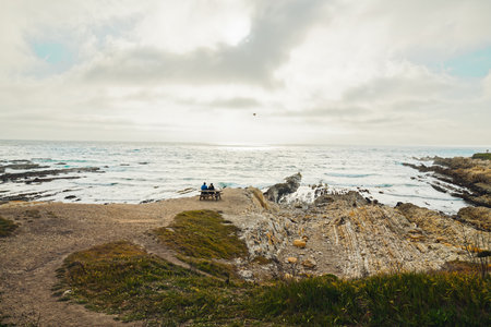 Los Osos, California, USA- April 17, 2021  Couple are sitting on the beach and enjoying the view, rocky cliffs and Pacific ocean with cloudy sky on background.  Montana de Oro State Park, California Central Coastのeditorial素材