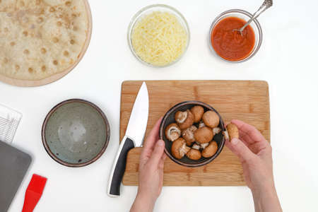 Crimini mushrooms in a bowl close up on kitchen table. Pizza with mozzarella and mushrooms recipe, flat lay, woman handsの写真素材