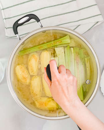 Woman hand puts lid on pan, close up view from above, vertical banner. Celery soup step by step recipeの写真素材