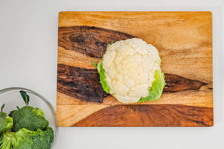 Cauliflower and broccoli close up on wooden cutting  board on light grey background, flat layの写真素材