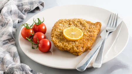 Crispy pan fried breaded pork chops served with lemon and fresh tomatoes close up on a plate on light grey backgroundの写真素材