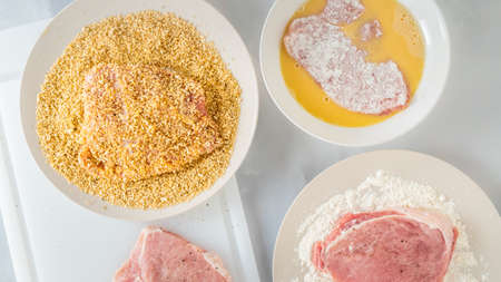 Breaded pork chops recipe. Pork chops on a plate with flour, eggs, and bread crumbs, close up view from aboveの写真素材