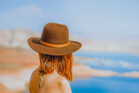 Red-haired woman wearing a hat on the beach overlooking lake, rear viewの写真素材