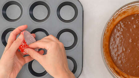 Chocolate muffins or chocolate cupcakes recipe. Chocolate batter in a bowl, and muffin pan with cupcake liners, close up view from above, woman handsの写真素材