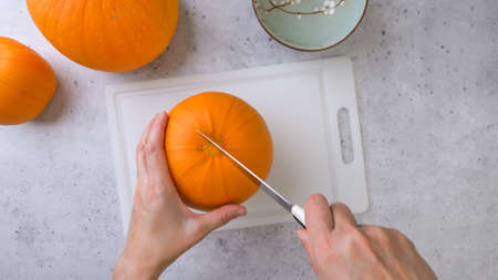 Woman cuts fresh raw yellow pumpkin on cutting board, close up view from above, copy spaceの写真素材
