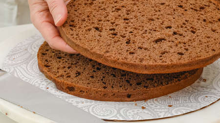 Assembling chocolate cake. Step by step baking process, close up view, woman hands, white kitchen...