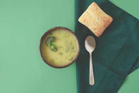 Broccoli cream soup in a bowl served with ciabatta roll close up on light green background, flat lay with copy space. Healthy organic vegetarian vegan diet fresh food.の写真素材