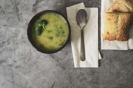 Broccoli cream soup in a bowl served with ciabatta rolls close up on gray rustic background, flat lay with copy space. Healthy organic vegetarian vegan diet fresh food.の写真素材