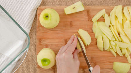 Woman slicing fresh peeled apples on a wooden cutting board, flat layの写真素材