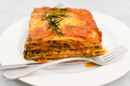 Spinach lasagna. Delicious spinach lasagna served with fresh rosamary close up on a plate on light grey backgroundの写真素材