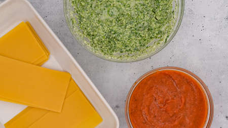Uncooked lasagna noodles, bowl of marinara sauce, and bowl of spinach mix close up on light grey background. Spinach lasagna step by step recipeの写真素材