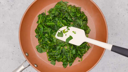 Mixing baby spinach on a frying pan. Close up view from above, copy spaceの写真素材