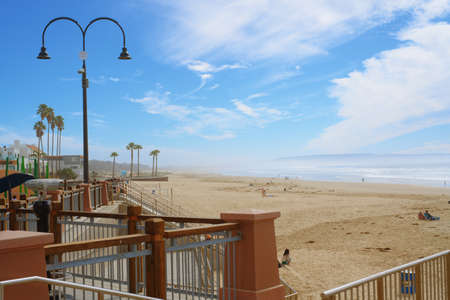 Pismo Beach, California, USA - March 3, 2022.  Pismo Beach wooden boardwalk, and wide sandy beach. Beautiful view of Pismo Beach city with mountains and cloudy sky on backgroundのeditorial素材