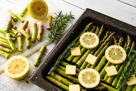 Fresh green asparagus, sliced lemon, and butter, fresh rosemary, and seasonig close up on baking...