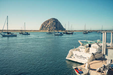 Morro Bay, California, USA - February 16, 2022.   Sailing boats moored in Morro Bay harbor. Beautiful Morro Rock and clear blue sky on backgroundのeditorial素材