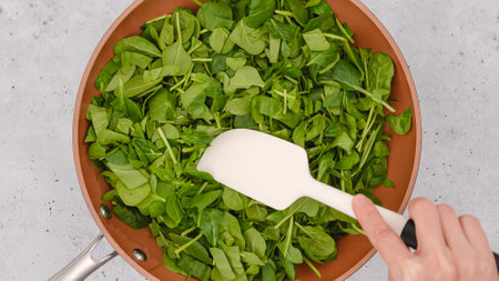 Woman mixing baby spinach on frying pan, flat lay, light grey background, copy spaceの写真素材