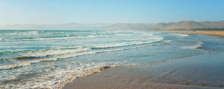 Wide sandy beach and ocean view. Beautiful seascape, mountains, and clear blue sky background, copy space, panoramic viewの写真素材