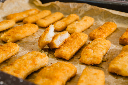 Crunchy breaded fish sticks made from wild caught Alaskan Pollock close-up on a baking pan, just...
