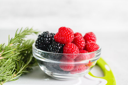 Galss bowl with fresh berries, and fresh rosemary close-up on the kitchen table in the light grey backgroundの写真素材