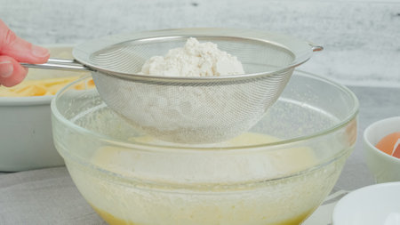Cake dough preparation process. Chef pouring or sifting flour in a glass bowl using a colander....
