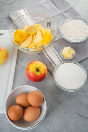 Baking pan with apple slices, eggs, sugar, and flour in bowls close-up on a kitchen table, vertical banner. Apple cake recipe, preparation processの写真素材