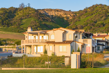 Shell Beach, California, USA - February 19, 2023. Beautiful houses with nicely landscaped front the yard, and green hills and clear blue sky in the background in a small beach town in California at sunsetのeditorial素材