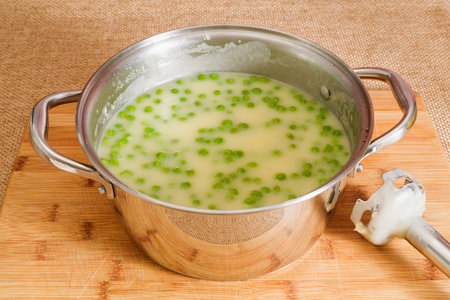 Celery cream soup with green pea close-up in a pan on rustic wooden backgroundの写真素材