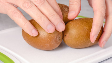 Golden kiwi close-up in woman hands. Tree ripe organic fruits on cutting boardの写真素材