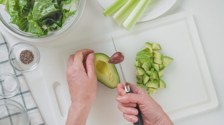 Woman removing the avocado pit. Green salad with celery, lettuce, and avocado recipe. Ingredients...