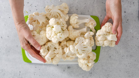 Cauliflower close-up on cutting board on kitchen table, woman hands, flat layの写真素材
