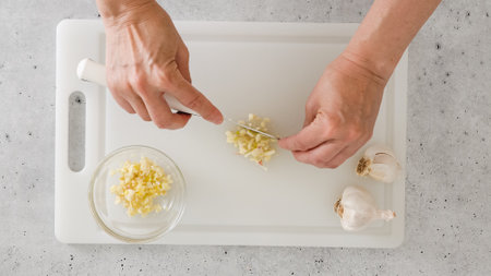 The chef chopping garlic on a white plastic cutting board, close-up view, preparation process,...