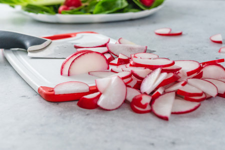 Sliced radishes on a white plastic cutting board on a light gray stone background, close-up viewの写真素材