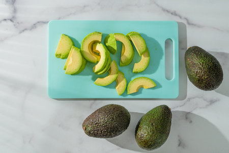 Avocado close-up on the kitchen table. Fresh sliced avocado on a cutting board on a marble...