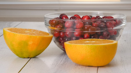 Fresh ripe cranberries in a glass bowl, and oranges close-up on kitchen tableの写真素材