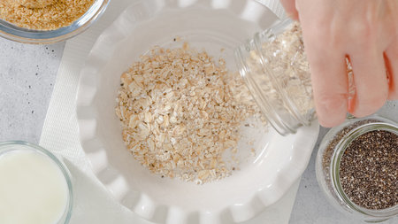 Woman preparing breakfast. Oatmeal made with whole grain oats, flaxseed meal, Chia seeds, and milk. Close up view from aboveの写真素材