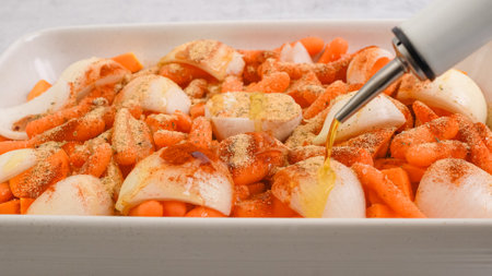 Roasted butternut squash soup recipe. Peeled and seedless squash cubes, carrot, onion, garlic, and spices close-up in a ceramic baking dish, topping with olive oilの写真素材