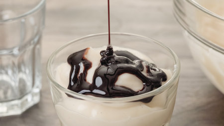 Topping white chocolate vanilla bean pudding with dark chocolate sauce. Close-up view of pudding in a glassの写真素材