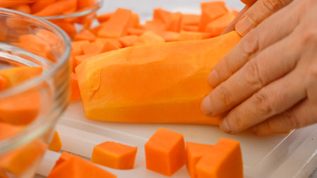 Butternut squash soup recipe. Cubes of a butternut squash close-up on a cutting board on the kitchen tableの写真素材
