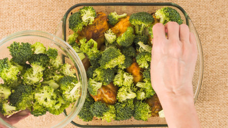 The chef hands put broccoli in a glass bowl with marinated chicken drumsticks. Close-up view from aboveの写真素材
