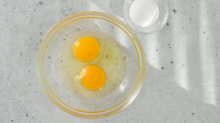 Raw eggs in a glass bowl, and salt in a glass bowl close-up on a light grey background, copy spaceの写真素材