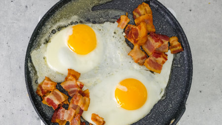 Two fried eggs and crispy fried bacon slices close-up on a hot frying pan. English breakfast recipe.の写真素材