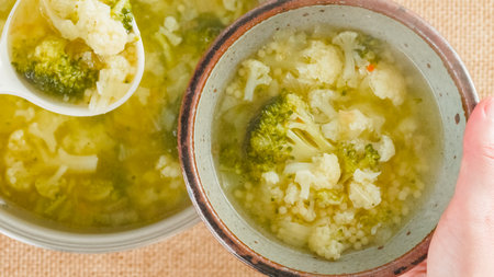 Woman serving soup. Cauliflower broccoli soup in a cooking pot and in bowls close-up on a table on a rustic background,の写真素材