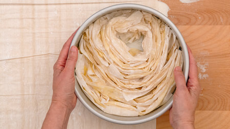 Phyllo dough pastry filled with cream cheese   recipe. Woman hands roll buttered dough layers, close-up baking process, flat lay, wooden backgroundの写真素材